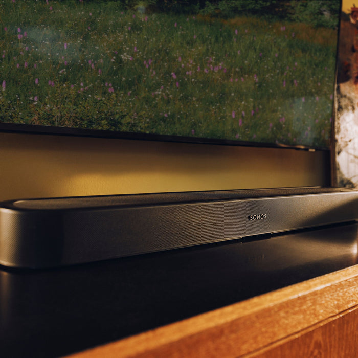 A black Sonos Beam Ultra soundbar positioned below a TV displaying a garden scene